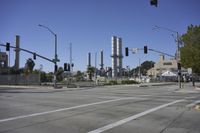 an empty street is near some factory smoke stacks and stop lights with a car coming to the top of it