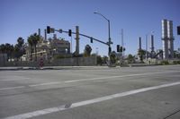 an empty street is near some factory smoke stacks and stop lights with a car coming to the top of it