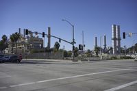 an empty street is near some factory smoke stacks and stop lights with a car coming to the top of it