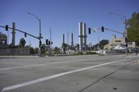 an empty street is near some factory smoke stacks and stop lights with a car coming to the top of it