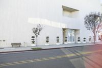 the empty street next to a modern white building with plants in the window pots, near the sidewalk in the city