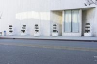 the empty street next to a modern white building with plants in the window pots, near the sidewalk in the city