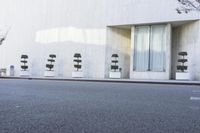 the empty street next to a modern white building with plants in the window pots, near the sidewalk in the city