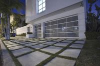 the large garage has glass windows and grass on it's front porch, which are a small patchy path near the sidewalk