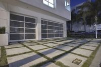 the large garage has glass windows and grass on it's front porch, which are a small patchy path near the sidewalk