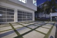 the large garage has glass windows and grass on it's front porch, which are a small patchy path near the sidewalk