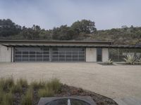 a garage with gray glass doors and a gravel path next to plants on the ground