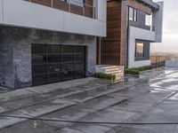 large modern home with wood and glass doors on concrete patio area next to two buildings