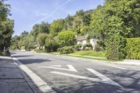 an empty suburban street has trees, bushes and houses on either side of the road