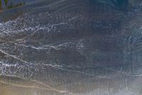 surfers stand on a beach with their boards in the ocean waves rolling towards the shore