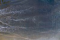 surfers stand on a beach with their boards in the ocean waves rolling towards the shore