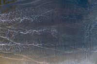 surfers stand on a beach with their boards in the ocean waves rolling towards the shore