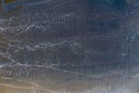 surfers stand on a beach with their boards in the ocean waves rolling towards the shore