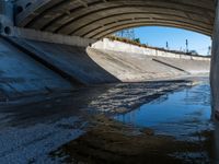 a water channel under an overpass and under construction with no water on it or one person in the way