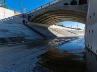 a water channel under an overpass and under construction with no water on it or one person in the way