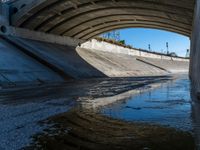 a water channel under an overpass and under construction with no water on it or one person in the way