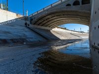 a water channel under an overpass and under construction with no water on it or one person in the way