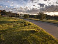 a paved road with grass and trees on each side of the street, between buildings and grassy fields