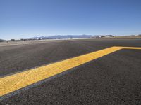 an empty airport runway in the desert with mountains in the background and a blue sky