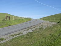 an empty country road with the side of a green grassy hill lined with fences and wires