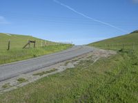 an empty country road with the side of a green grassy hill lined with fences and wires