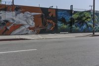a graffiti filled wall with a skeleton holding two swords on it near an intersection and a light pole