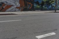 a graffiti filled wall with a skeleton holding two swords on it near an intersection and a light pole