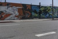 a graffiti filled wall with a skeleton holding two swords on it near an intersection and a light pole