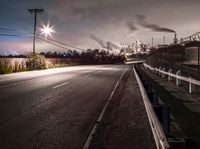 a dark highway and large factory plant is shown at night time, looking from underneath