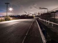 a dark highway and large factory plant is shown at night time, looking from underneath