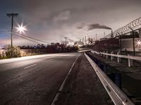 a dark highway and large factory plant is shown at night time, looking from underneath