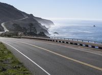 the road leads to a winding beach next to the ocean and cliffs with mountains on both sides