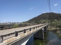 a view from a bridge overlooking trees and a mountain range of hills behind a bridge