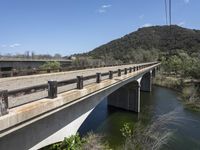 a view from a bridge overlooking trees and a mountain range of hills behind a bridge