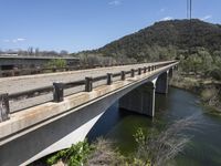 a view from a bridge overlooking trees and a mountain range of hills behind a bridge