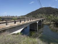 a view from a bridge overlooking trees and a mountain range of hills behind a bridge