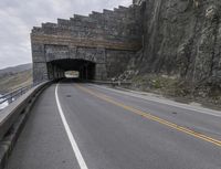 a tunnel and road running into the ocean with an ocean in the background on a gloom day