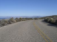 the empty road is surrounded by brush and sand and mountains in the distance in the desert