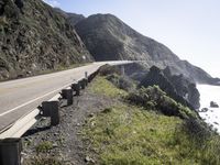 a scenic stretch of highway leading to the ocean near rocky coastline and cliffs on one side of the road with lots of green grass on both sides