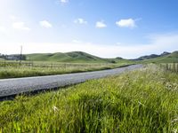 a person riding a bike down a long road in a grassy field next to a hillside