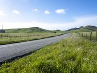 a person riding a bike down a long road in a grassy field next to a hillside