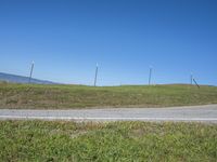 a blue sky and clouds above an empty road with several pole fenced areas on the hill side