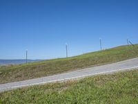 a blue sky and clouds above an empty road with several pole fenced areas on the hill side