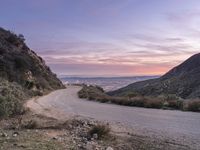 a view of the road in front of a hilly area and mountain range at dusk