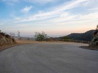 an empty road near the mountain overlooking water and hills with a lone dog walking in the distance