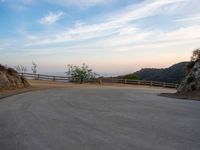 an empty road near the mountain overlooking water and hills with a lone dog walking in the distance