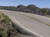 a mountain and road on an overpass with a man walking by it that has a yellow arrow painted into it