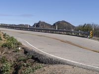 a mountain and road on an overpass with a man walking by it that has a yellow arrow painted into it