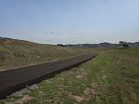 a long asphalt road going over the mountains to a grassy hill with a blue sky