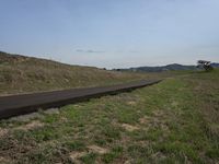 a long asphalt road going over the mountains to a grassy hill with a blue sky